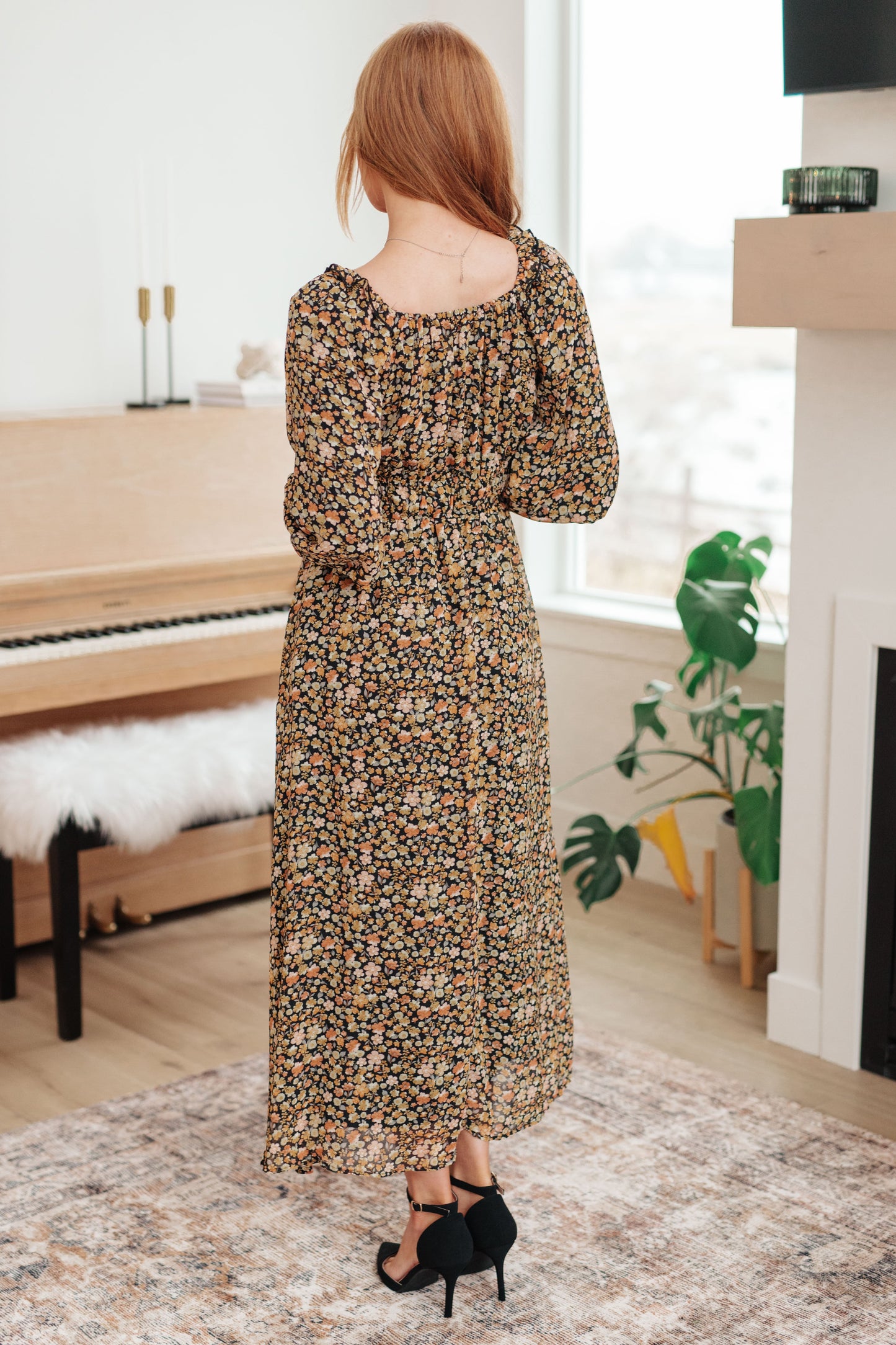 Woman in a floral dress standing in a room with a piano and window.