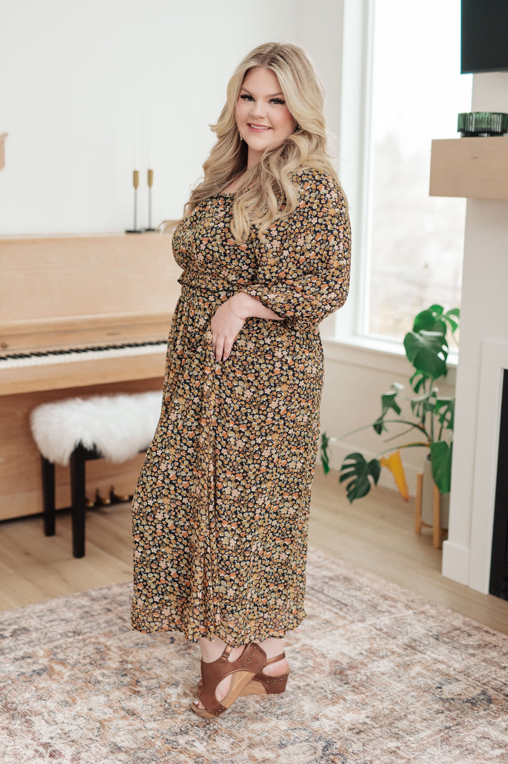 Woman in a floral dress standing in a room with a piano and plants.