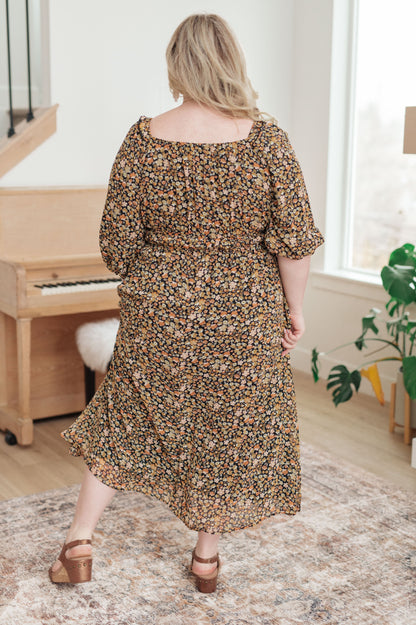 Woman in a floral dress standing in a room with a piano and window.