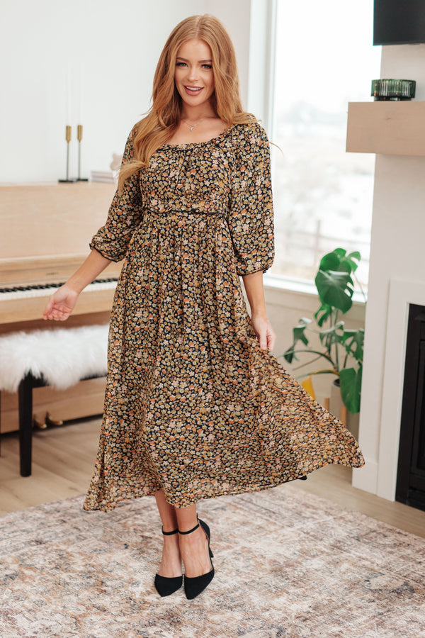 Woman in a floral dress standing in a room with a piano and window.