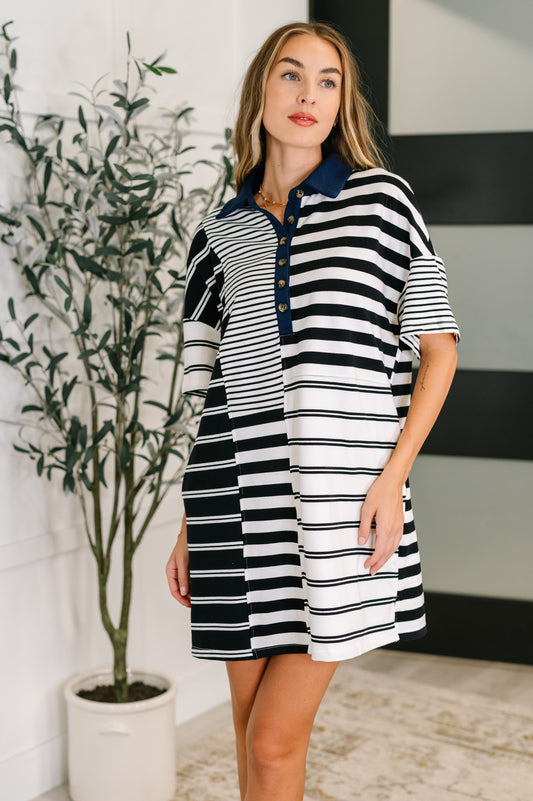 Woman wearing a black and white striped dress standing indoors with a plant in the background