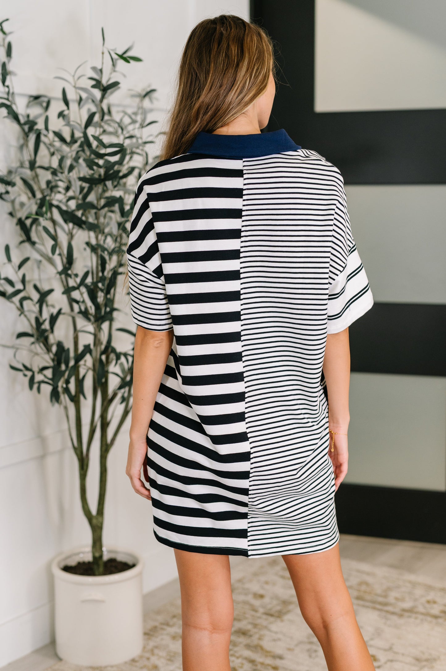 Woman wearing a black and white striped dress standing in a room with a plant and wall art.