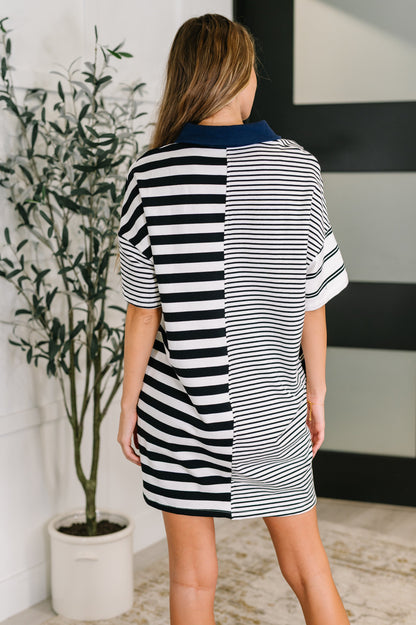 Woman wearing a black and white striped dress standing in a room with a plant and wall art.