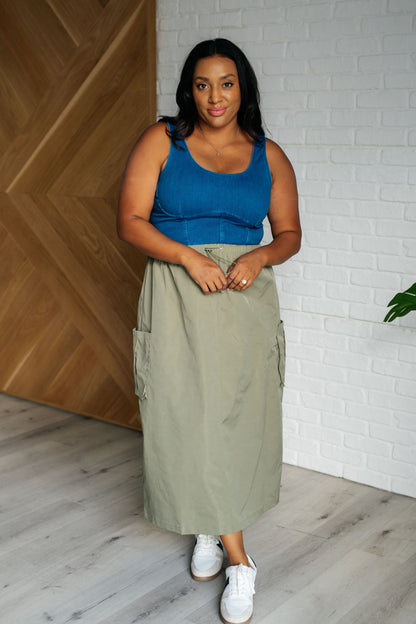 Woman wearing a blue top and green skirt standing against a white brick wall.