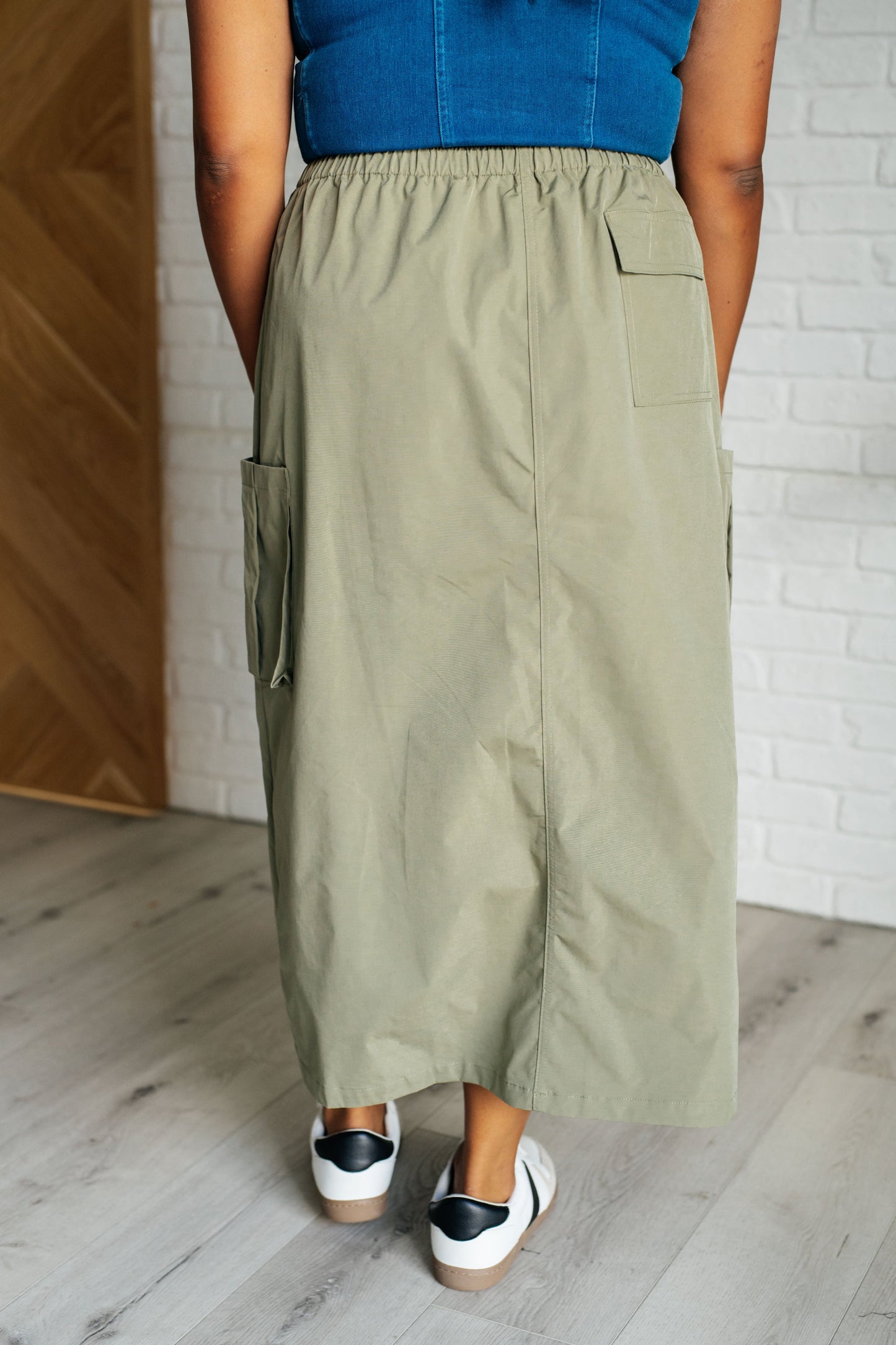 Person wearing a blue top and green wide-leg pants standing against a white brick wall.