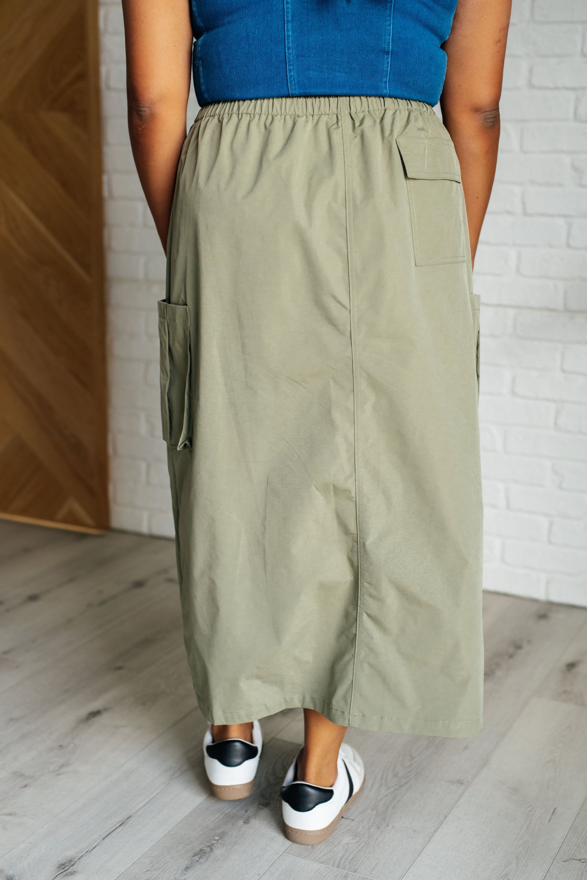 Person wearing a blue top and green wide-leg pants standing against a white brick wall.