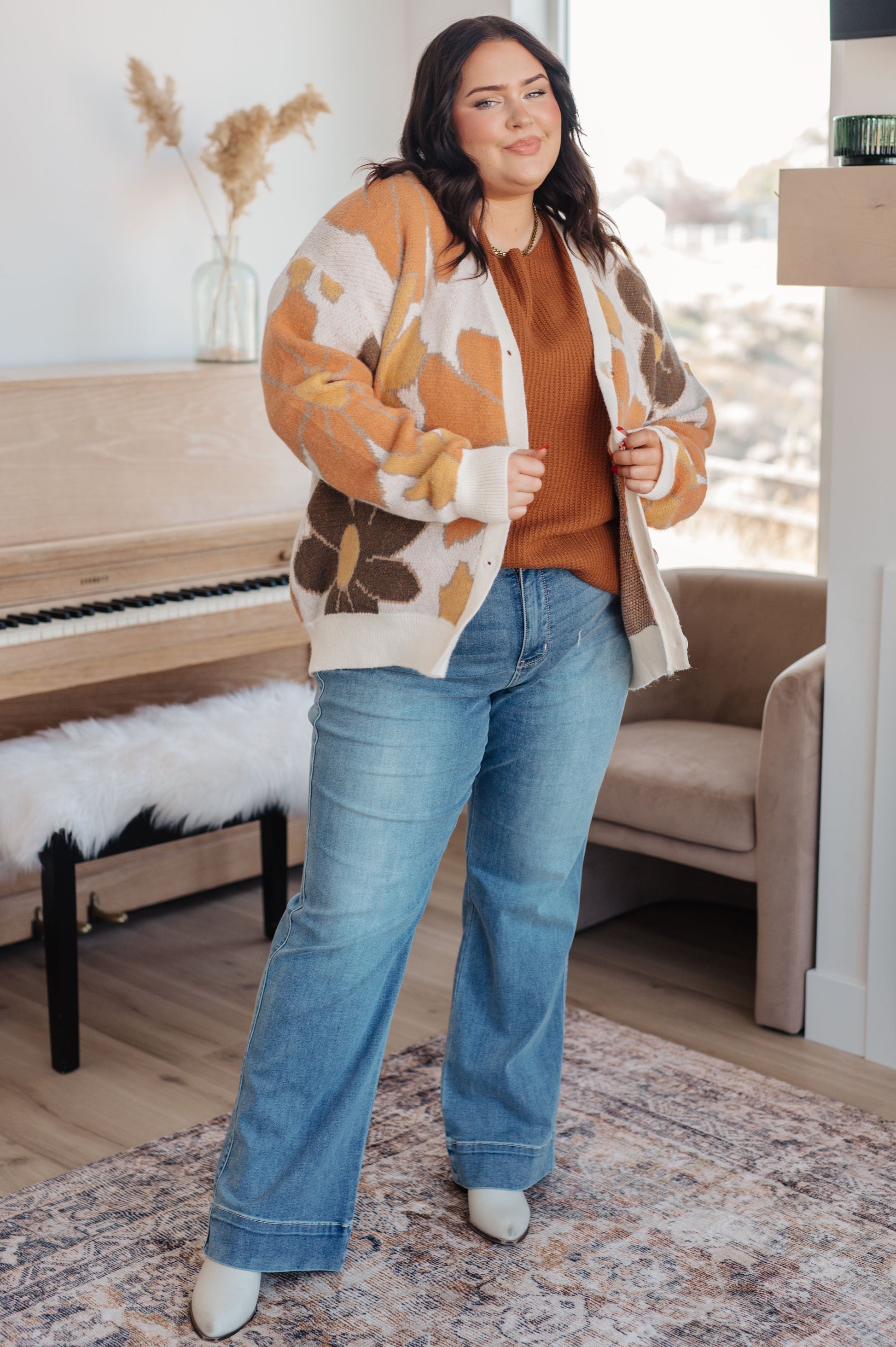 Woman wearing a patterned cardigan and jeans in a living room setting