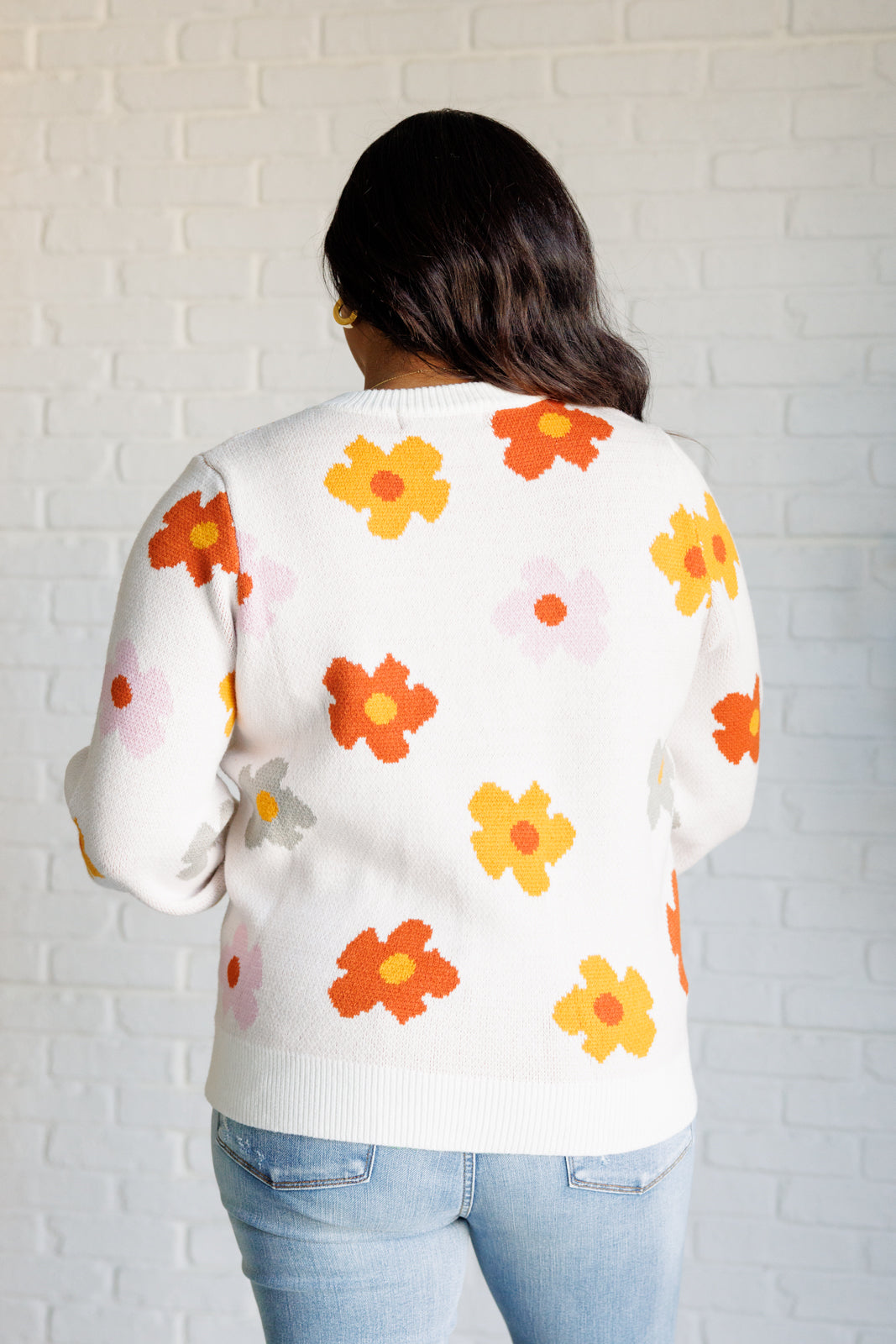 Person wearing a white sweater with colorful floral patterns against a white brick wall.