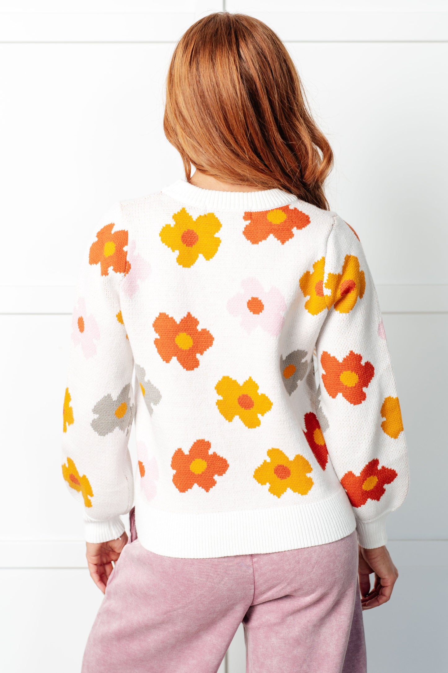 Person wearing a white sweater with colorful floral patterns on a white background