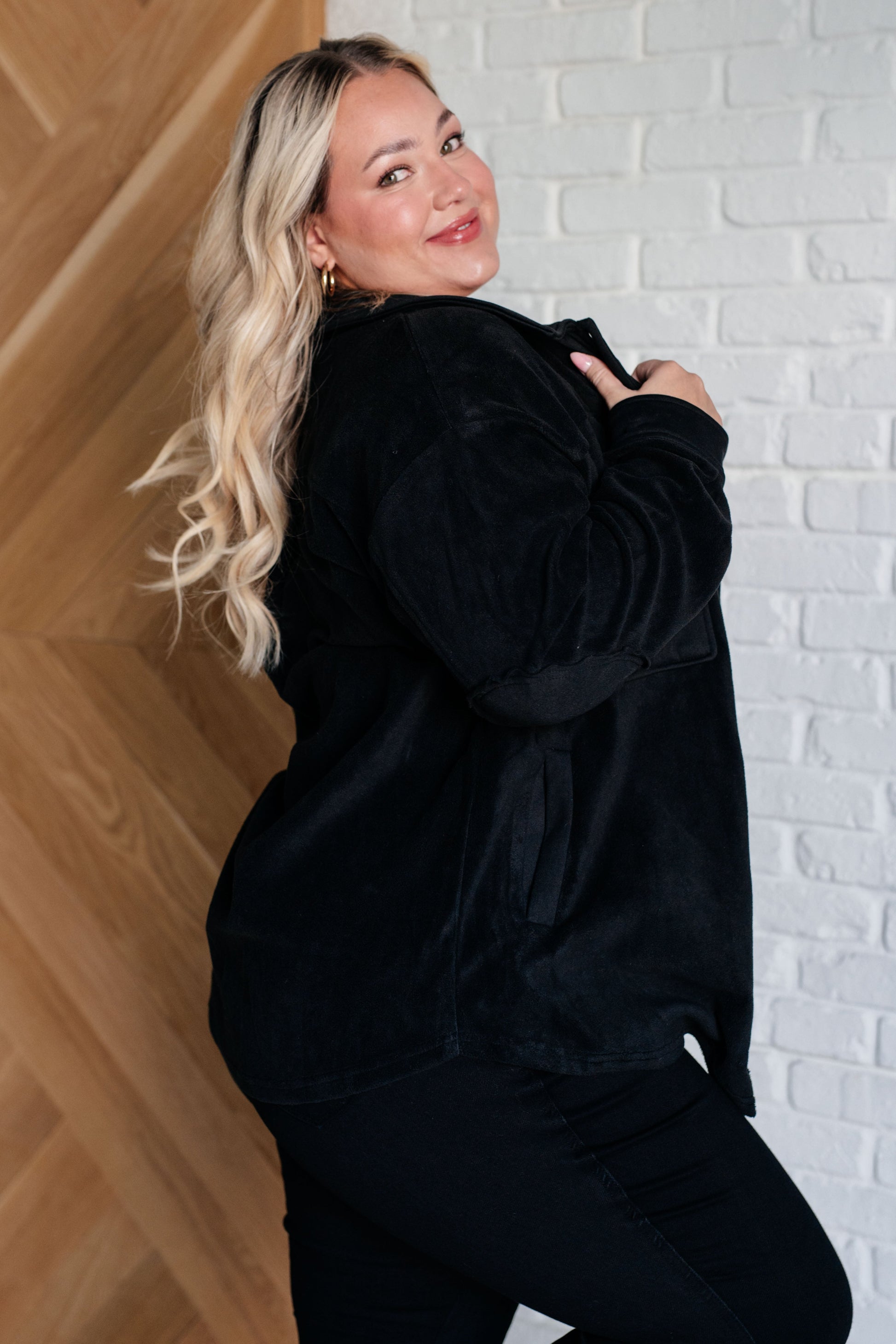 Woman wearing a black outfit against a white brick wall.