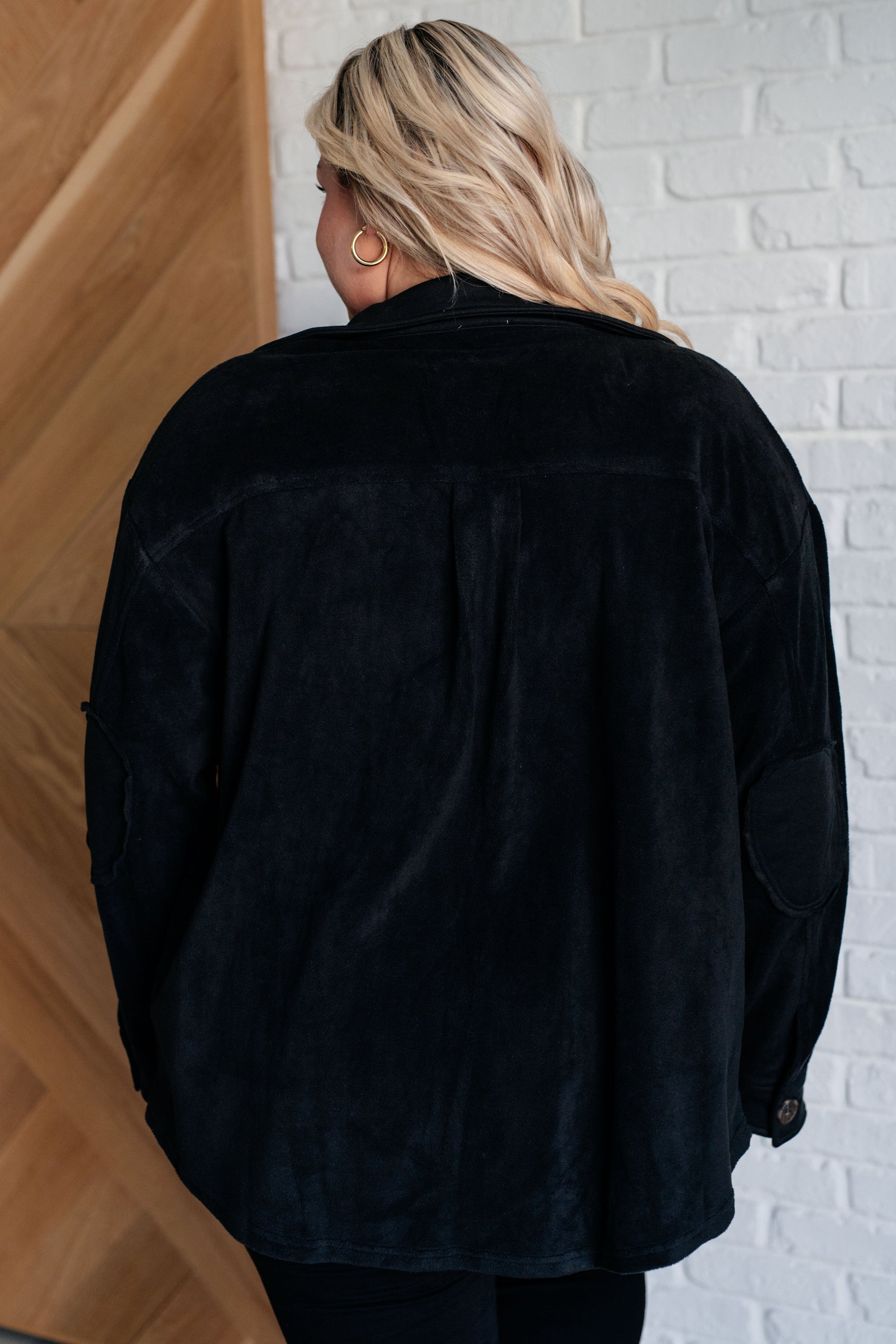 Person wearing a black jacket standing against a white brick wall.