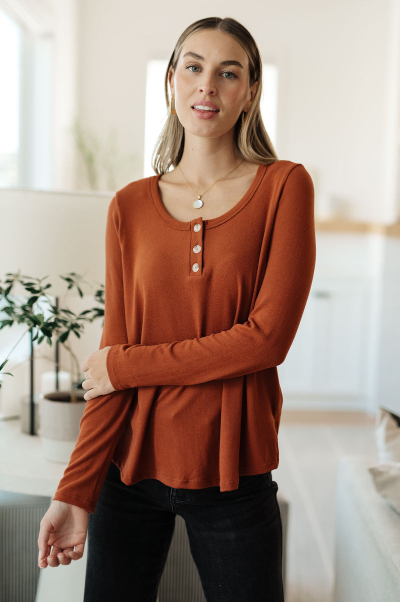 Woman wearing a rust-colored long-sleeve top in a bright room.