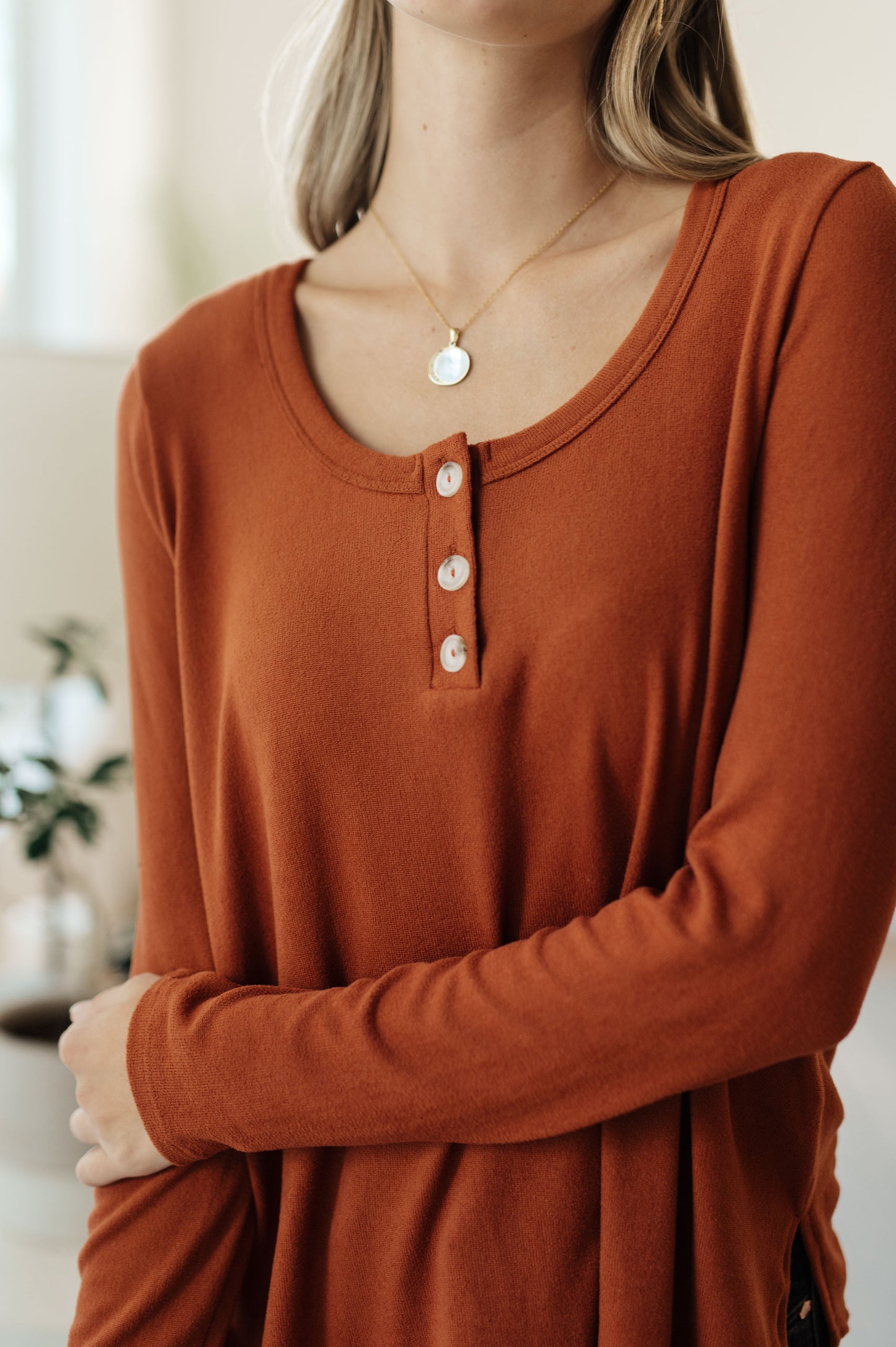 Person wearing a rust-colored long-sleeve shirt with buttons, standing indoors.