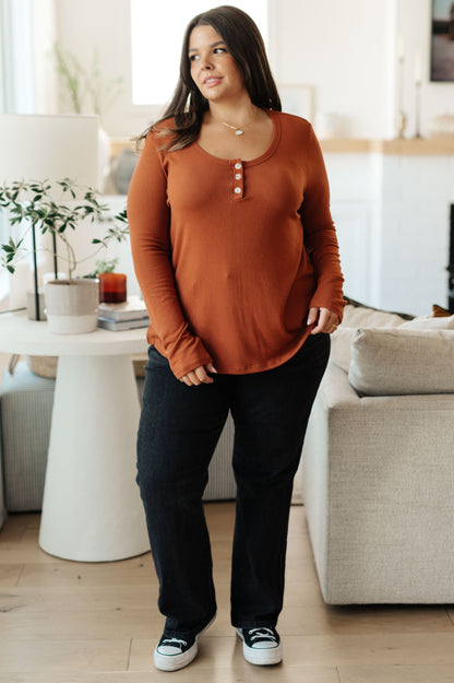 Woman wearing a rust-colored long-sleeve top and black pants in a living room.