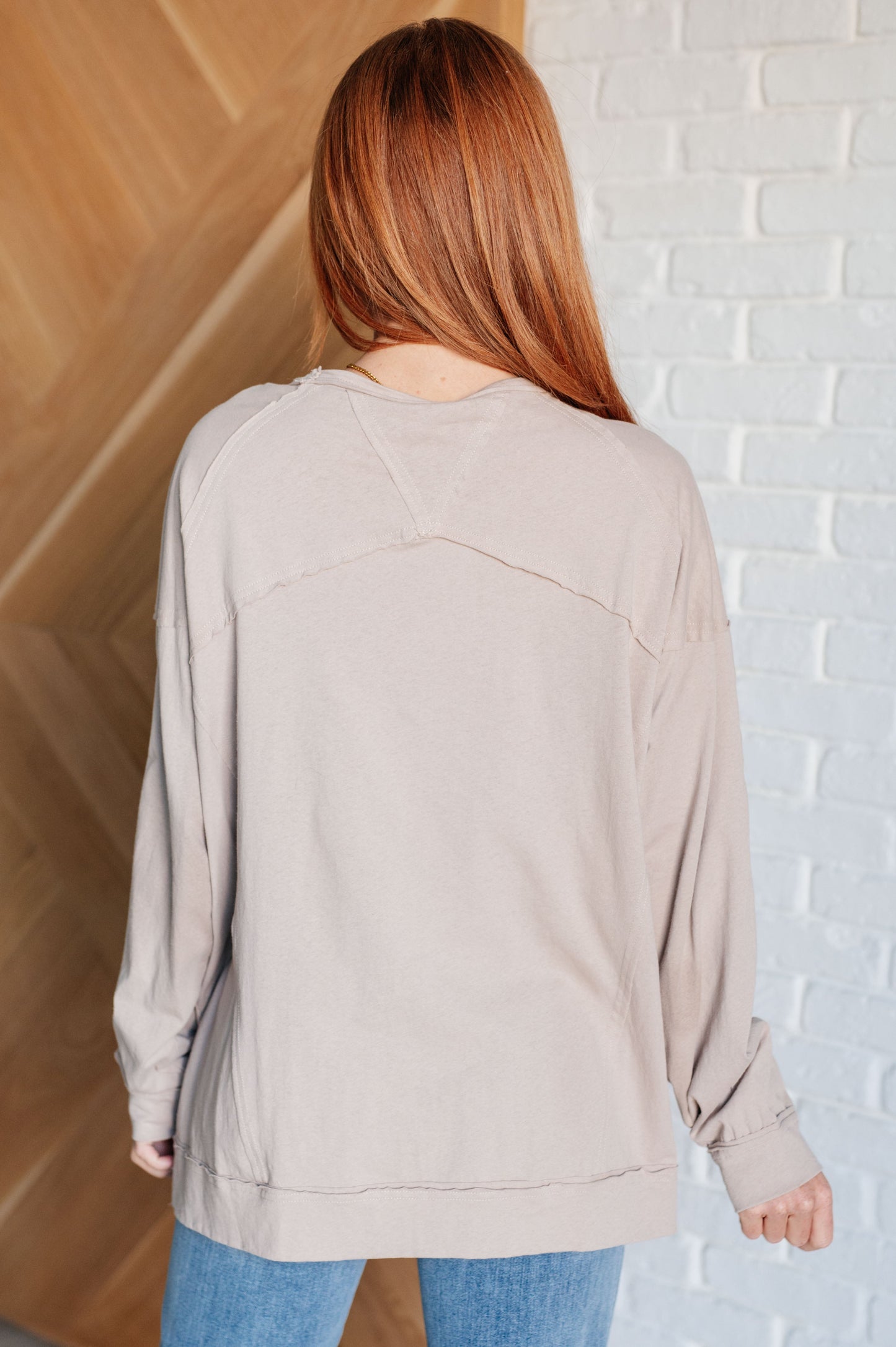 Person wearing a beige sweater standing against a white brick wall.