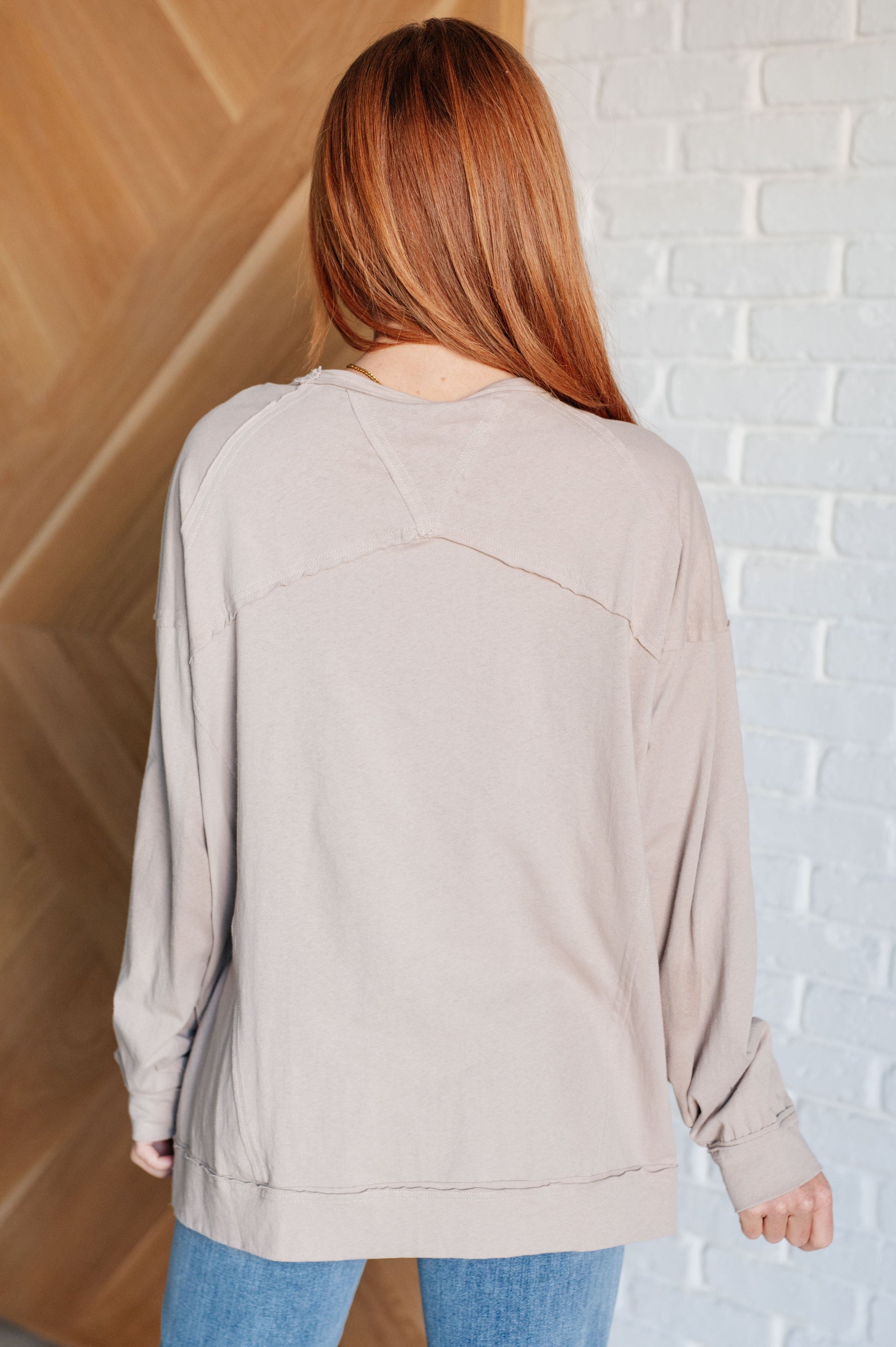 Person wearing a beige sweater standing against a white brick wall.