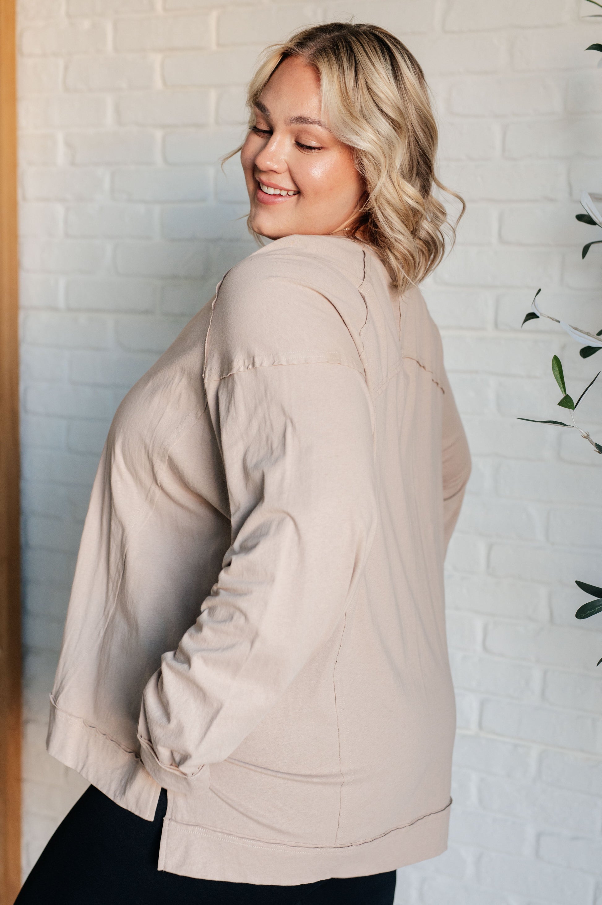 Woman wearing a beige jacket standing against a white brick wall.