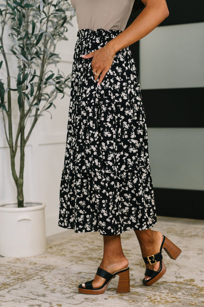 Person wearing a black and white floral skirt with a neutral background