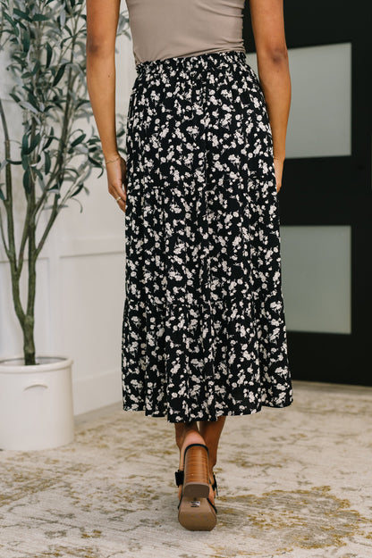 Person wearing a black floral skirt with a neutral background