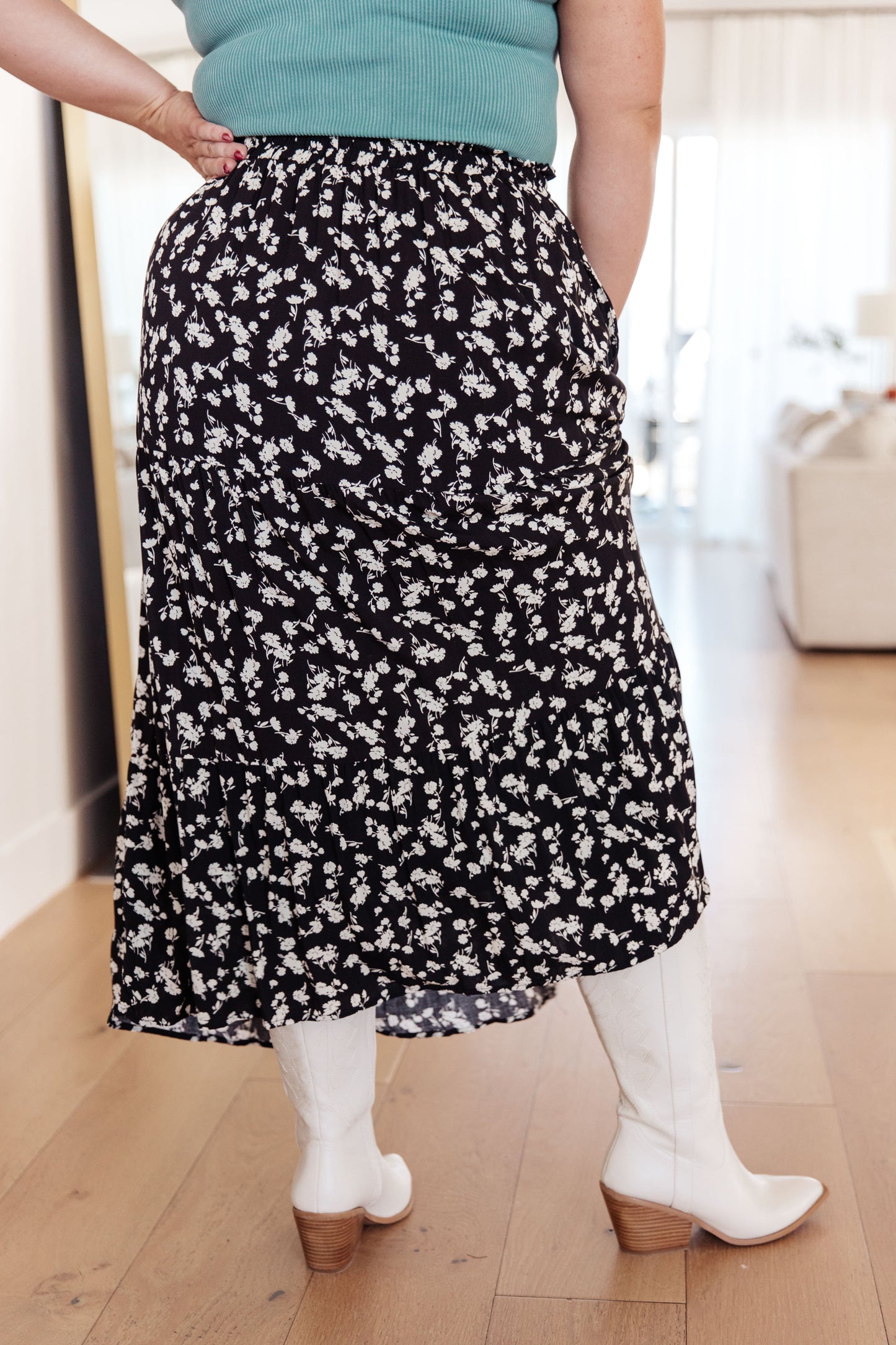 Person wearing a black floral skirt with white boots indoors.