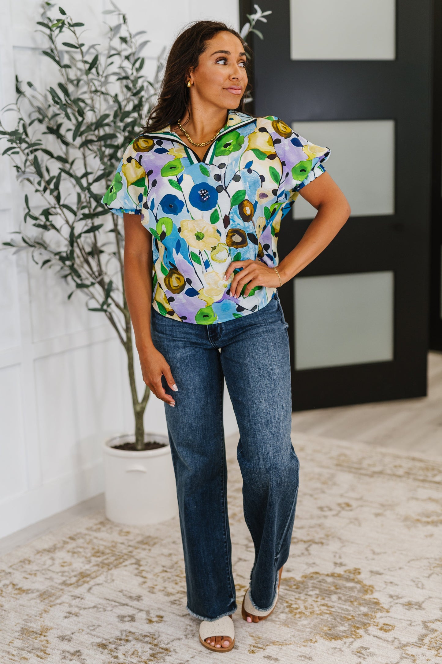 Woman wearing a colorful floral blouse and blue jeans indoors.