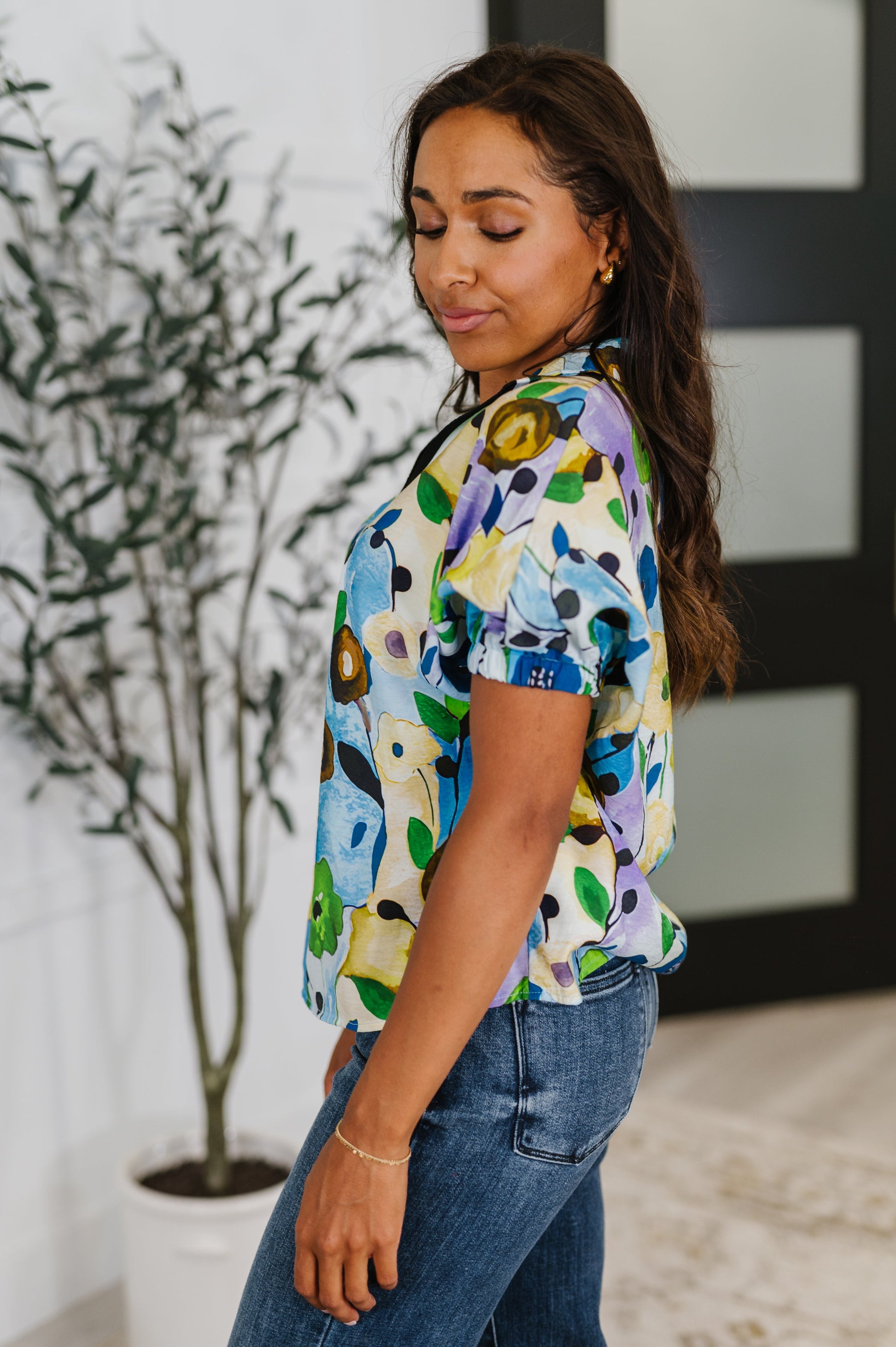 Woman wearing a colorful floral blouse and blue jeans indoors.