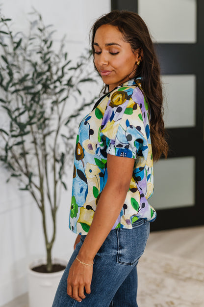 Woman wearing a colorful floral blouse and blue jeans indoors.