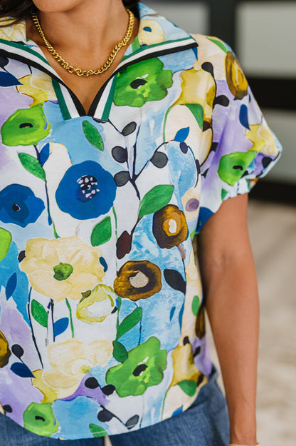 Colorful floral-patterned shirt worn by a person, with a blurred indoor background.