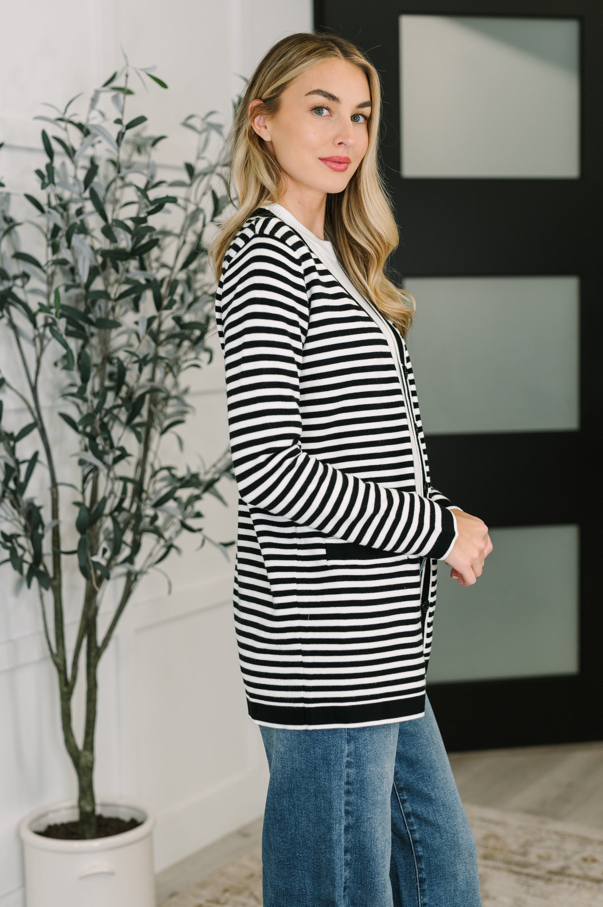 Woman wearing a black and white striped sweater and blue jeans indoors.