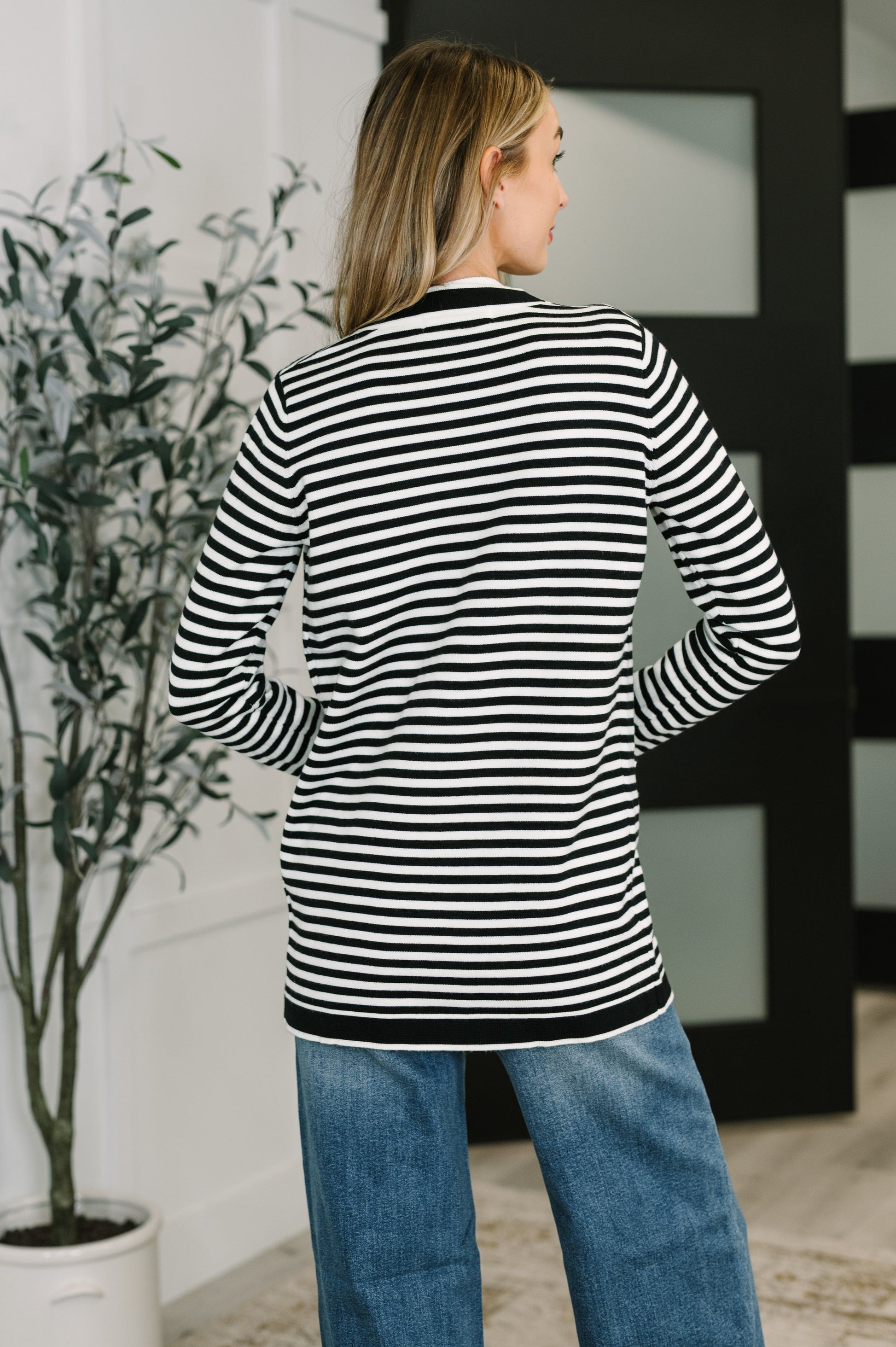 Woman wearing a black and white striped shirt and blue jeans, standing indoors.