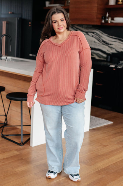 Woman wearing a pink sweater and light blue jeans standing in a kitchen.