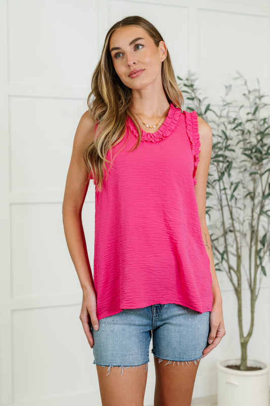 A model wearing a hot pink sleeveless tank top with ruffle detail at the neckline, paired with blue denim shorts.