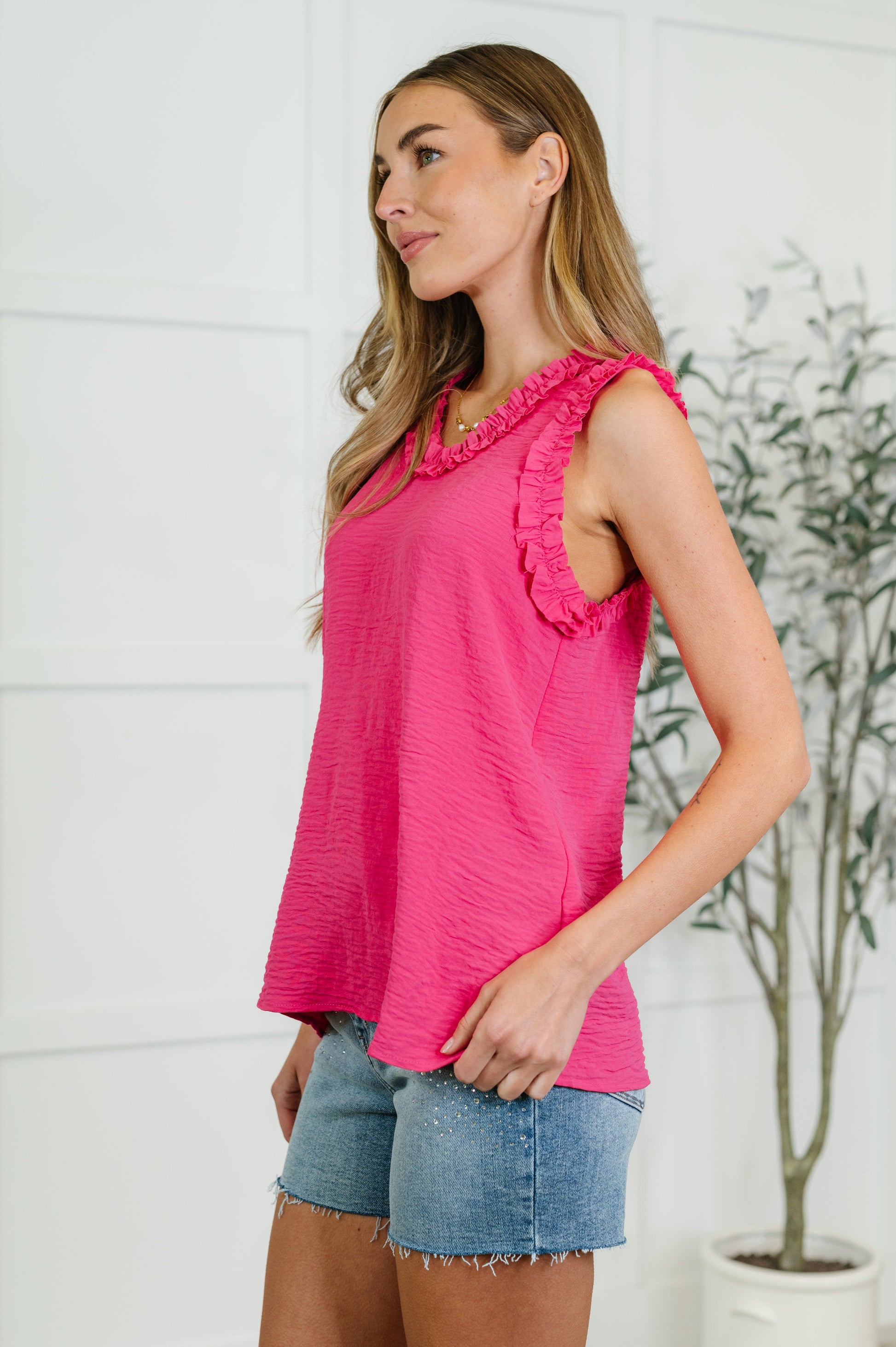 Woman wearing a pink sleeveless top and denim shorts in a bright setting.