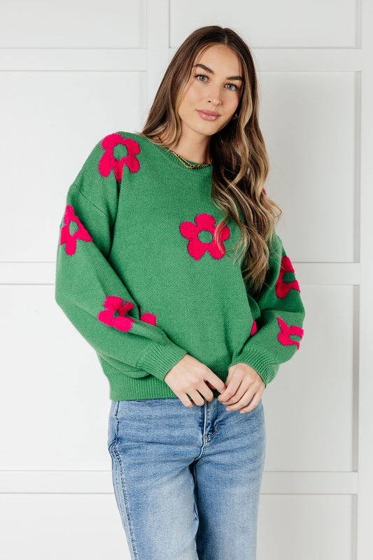 Woman wearing a green sweater with pink floral patterns against a white wall.