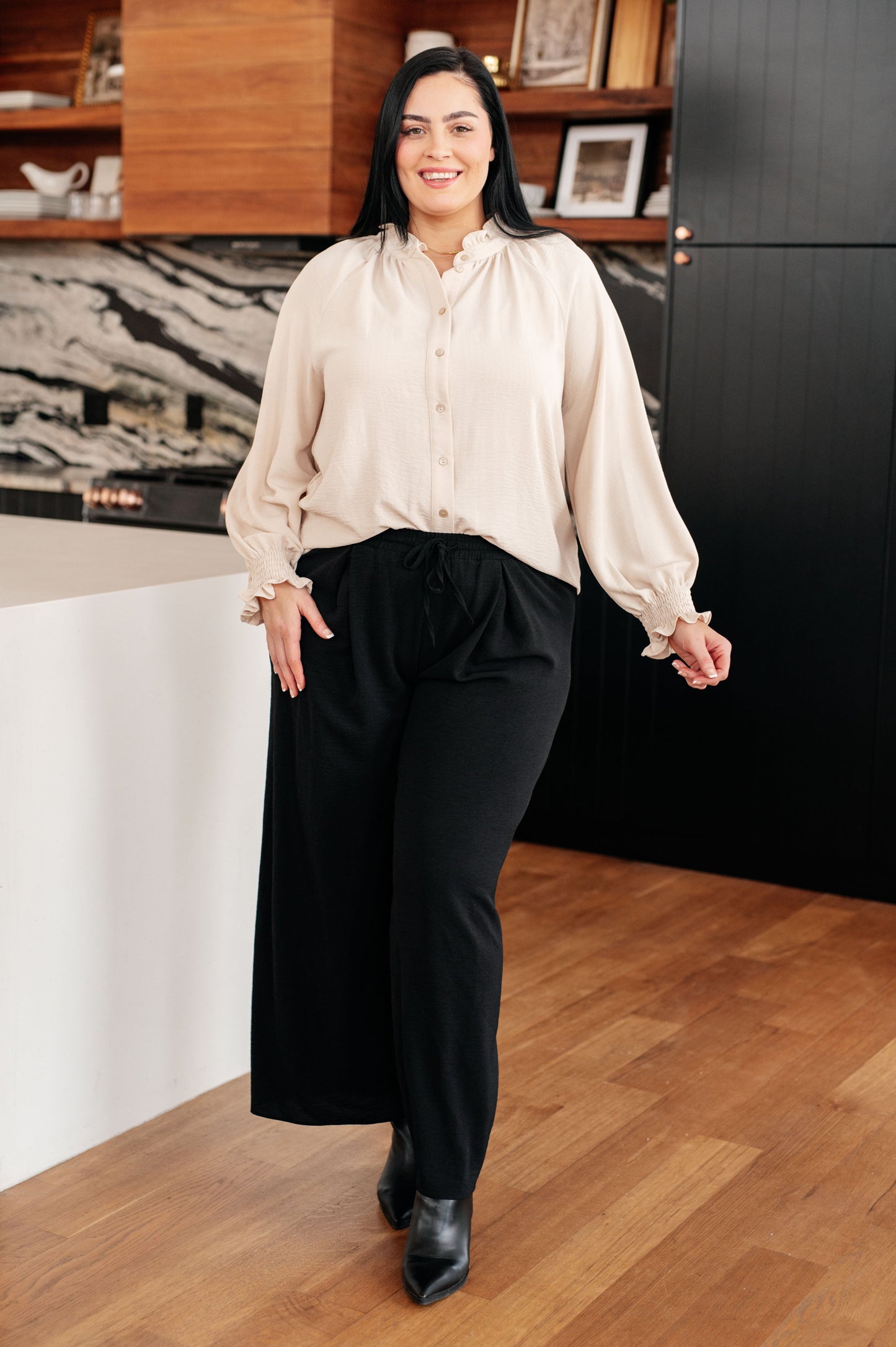 Woman in a beige blouse and black pants standing in an office setting.