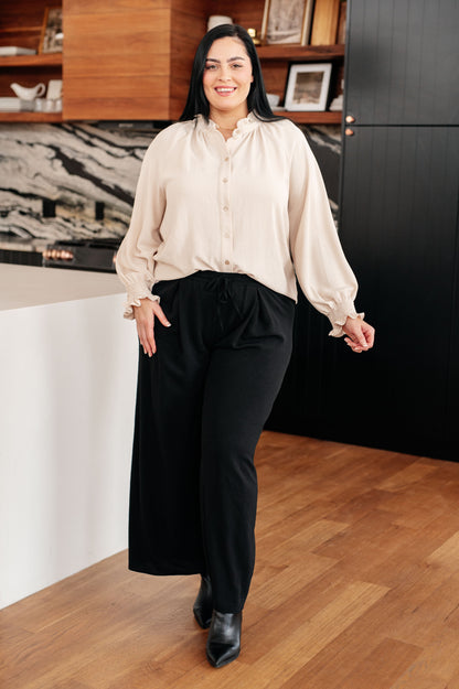Woman in a beige blouse and black pants standing in an office setting.