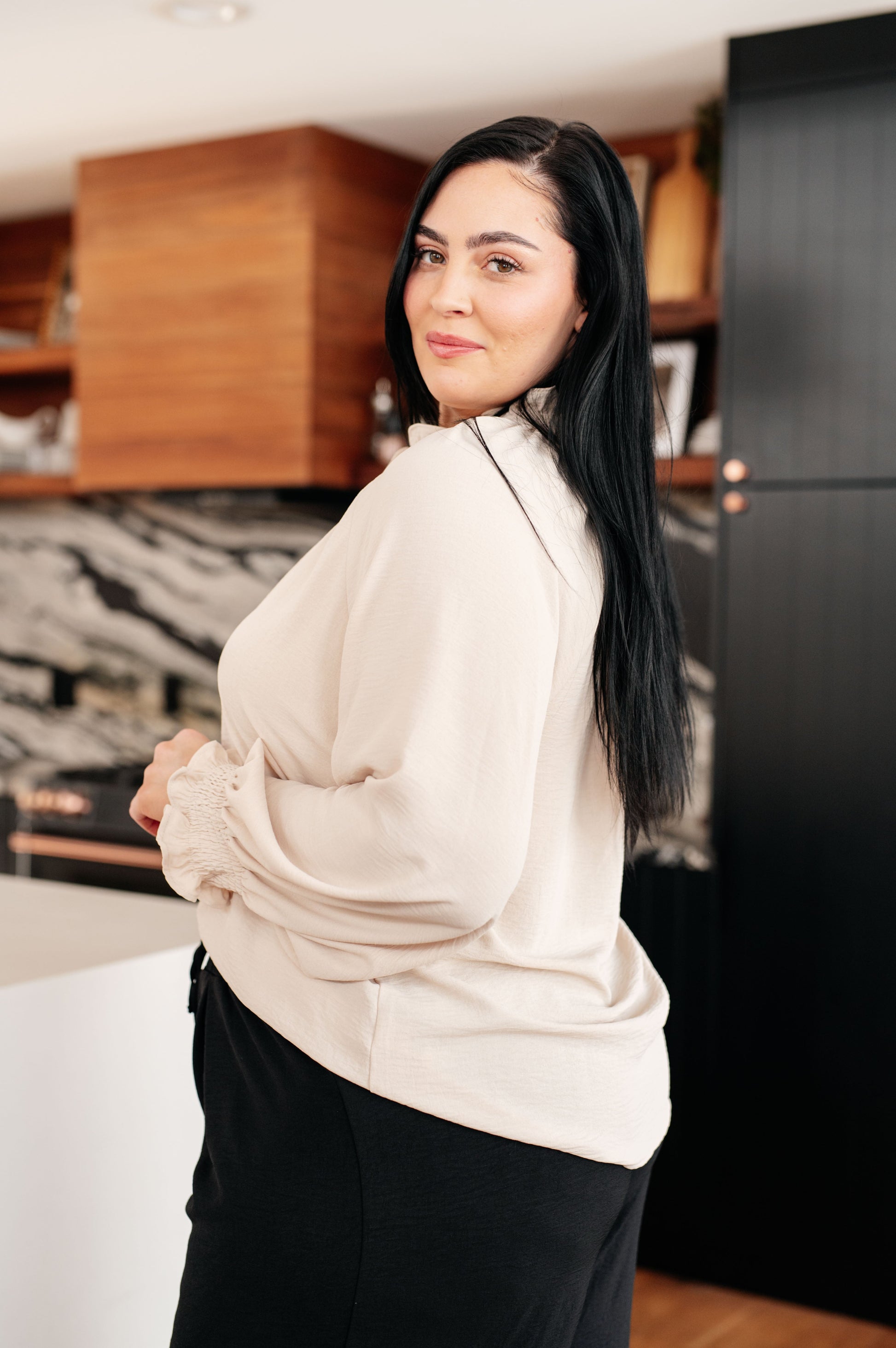 Woman in a beige sweater standing in a modern kitchen.