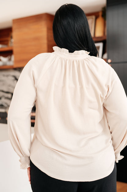 Person wearing a beige blouse with long sleeves in an indoor setting