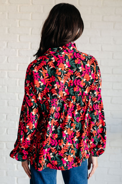 Person wearing a colorful floral blouse against a white brick wall.