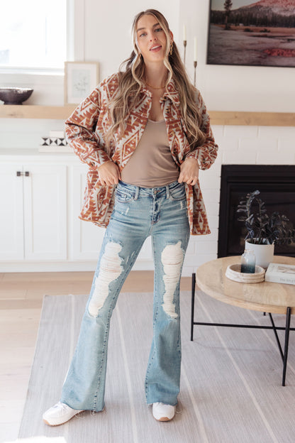 Woman wearing a patterned jacket, beige top, and distressed jeans in a kitchen.