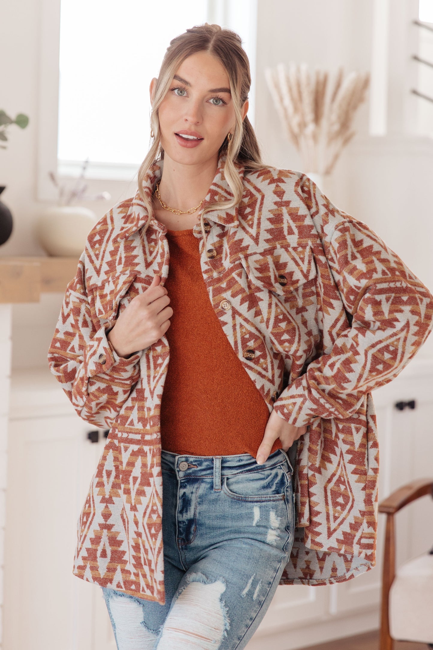 Woman wearing a patterned jacket over a sweater and jeans in a bright room.