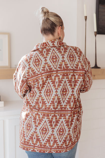 Person wearing a patterned jacket in a room with white walls and wooden furniture.