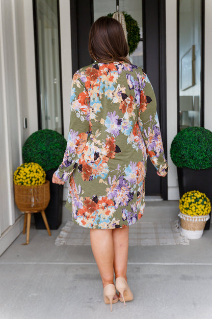 Person wearing a floral dress standing on a porch with decorative plants.