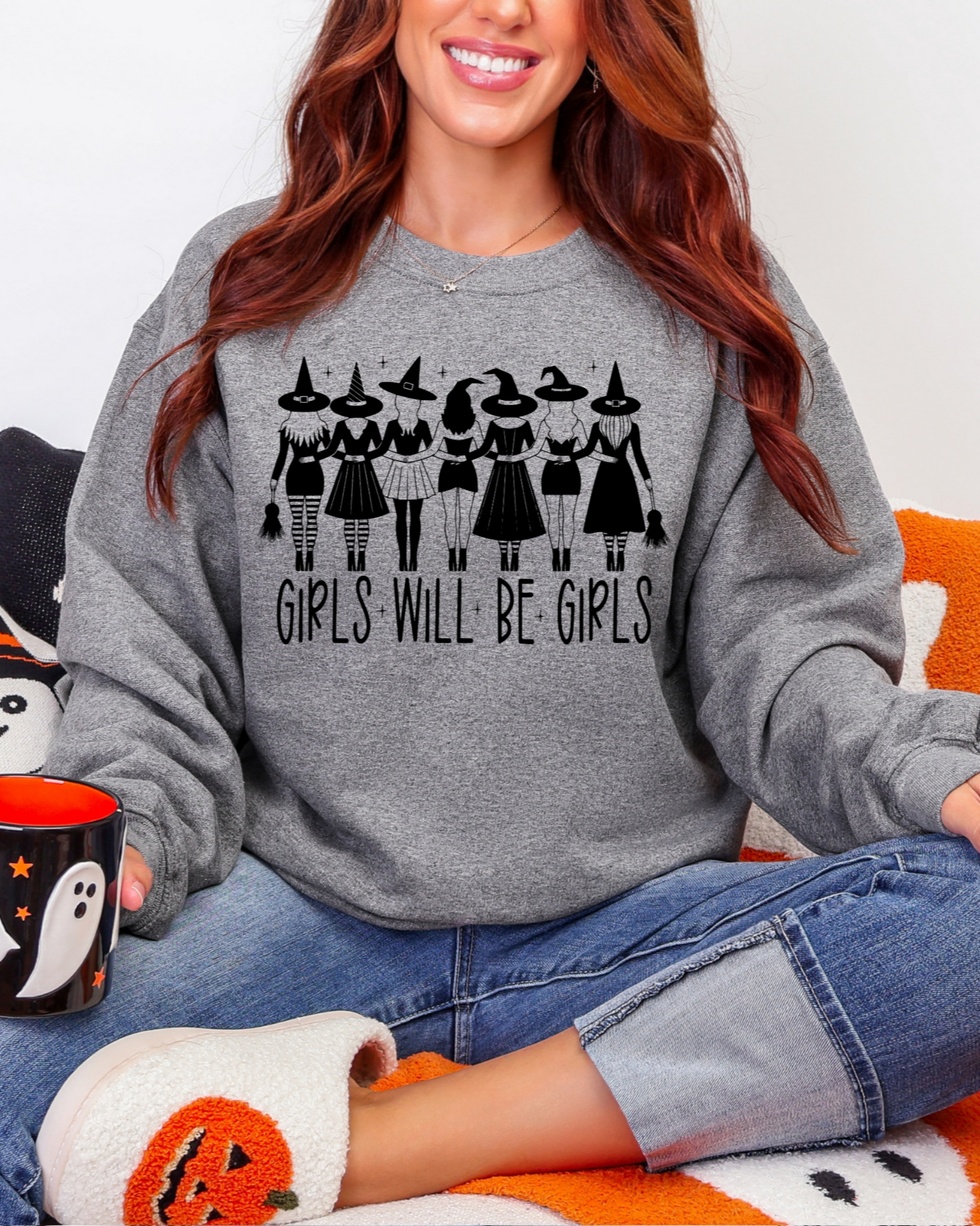 Person wearing a gray sweatshirt with 'Girls Will Be Girls' text, sitting on an orange and white blanket.