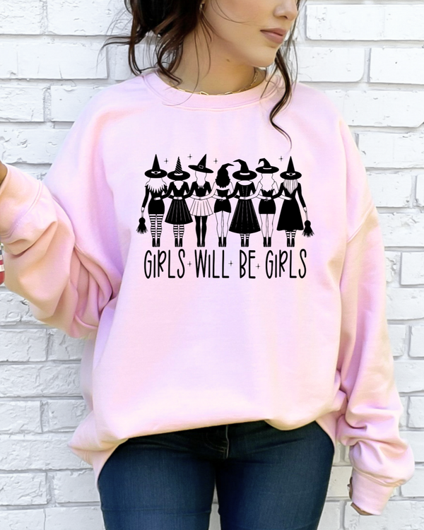 Person wearing a pink sweatshirt with 'Girls Will Be Girls' text and graphic, holding a colorful drink.