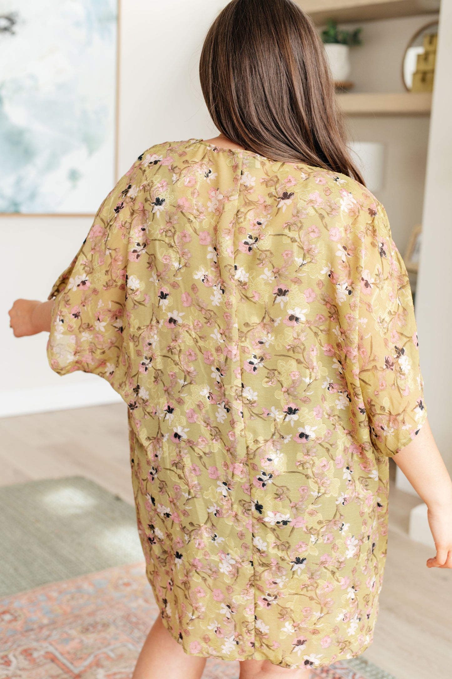 Woman wearing a floral kimono-style garment indoors.