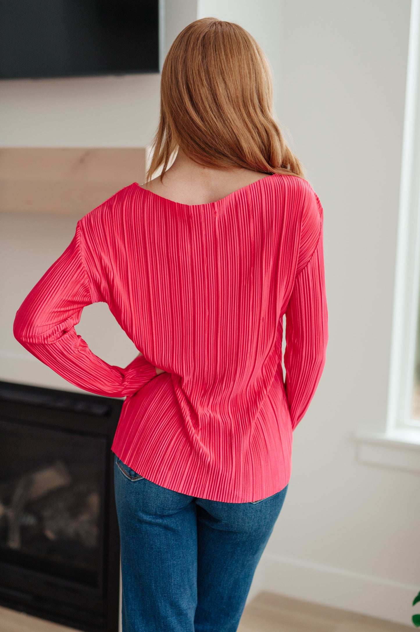 Person wearing a bright pink pleated top and blue jeans indoors.