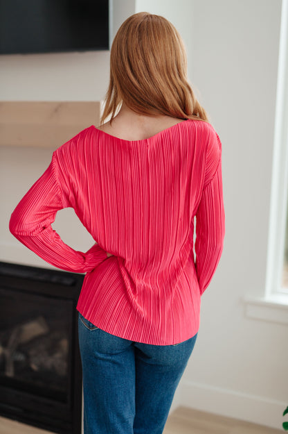 Person wearing a bright pink pleated top and blue jeans indoors.