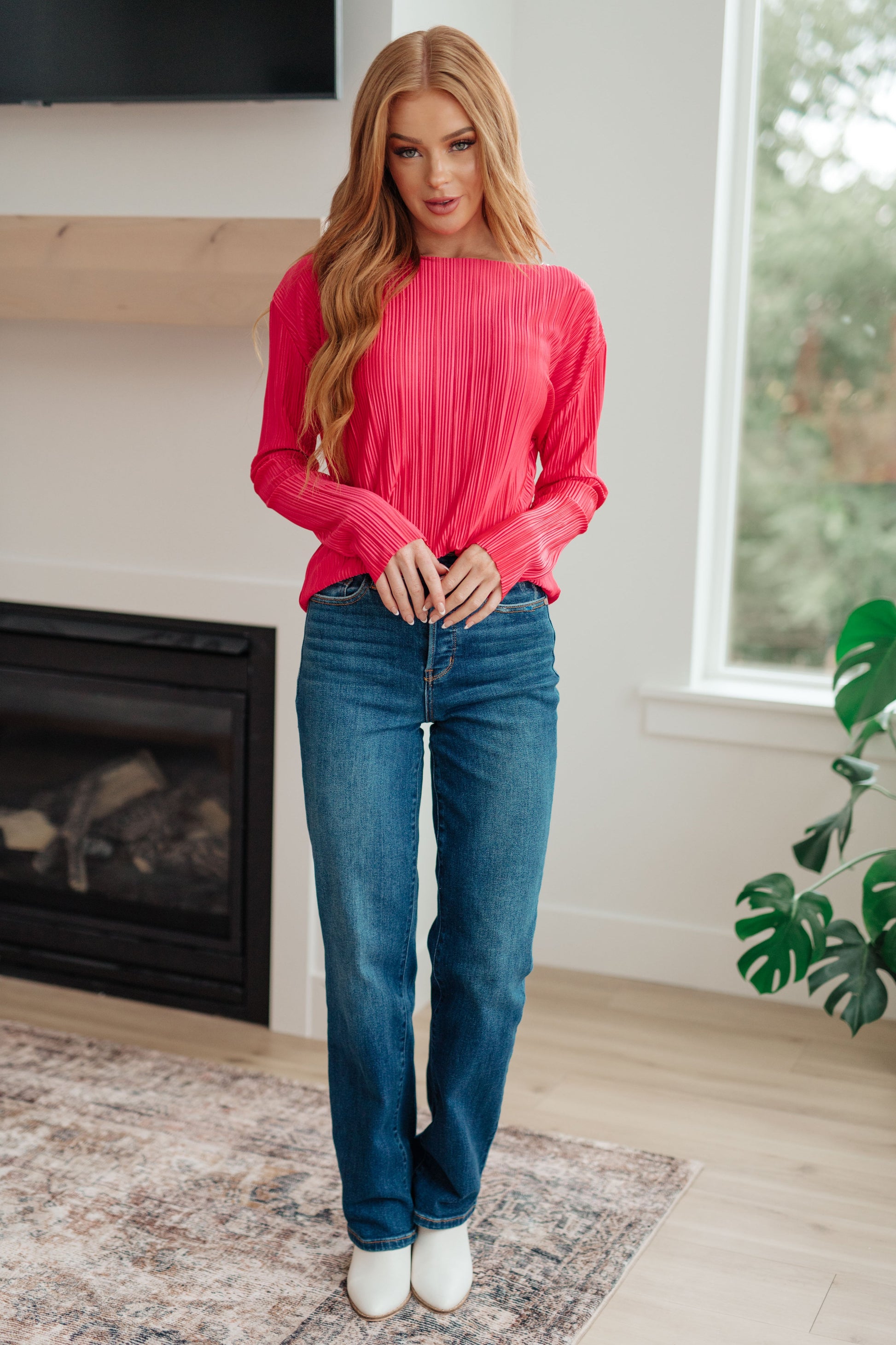 Woman wearing a pink sweater and blue jeans standing in a living room.