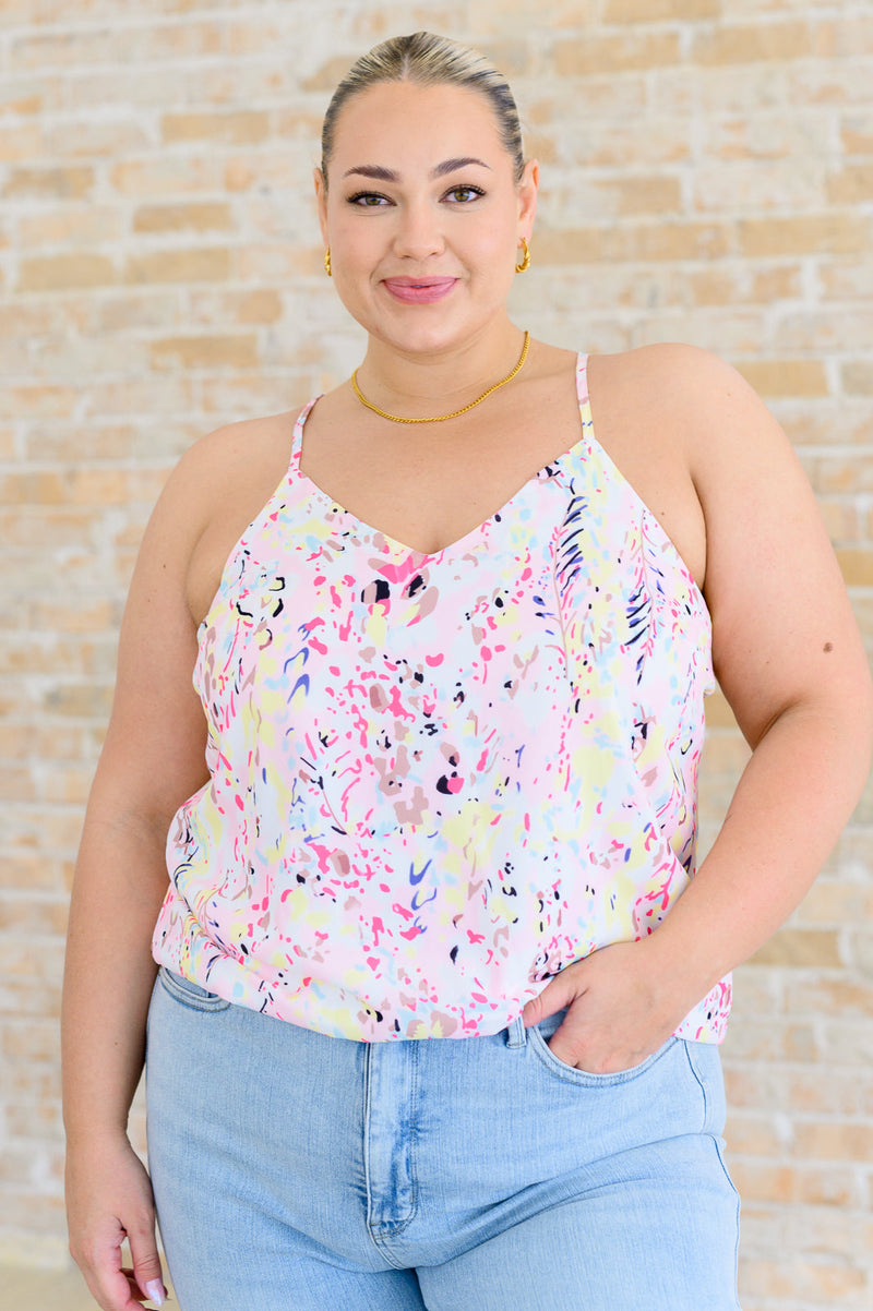 A woman wearing a multicolor printed camisole top with a v-neckline and adjustable straps, paired with high-rise straight jeans.